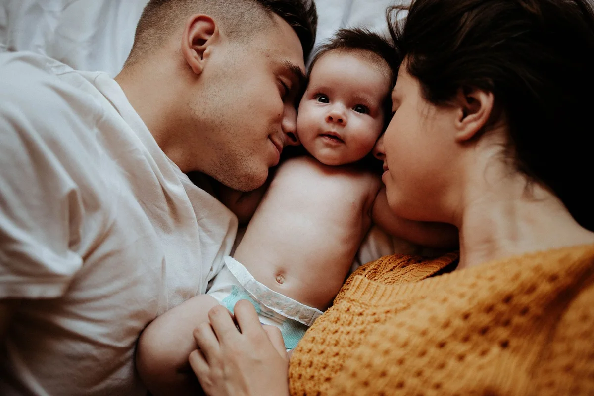 Two parents cuddling their newborn baby together at home