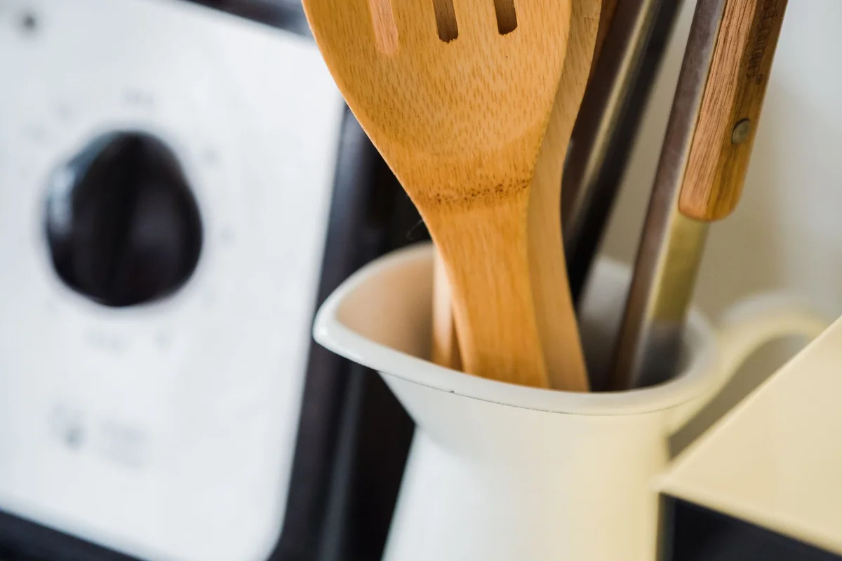 Wooden and metal cooking utensils in a white kitchen utensil holder