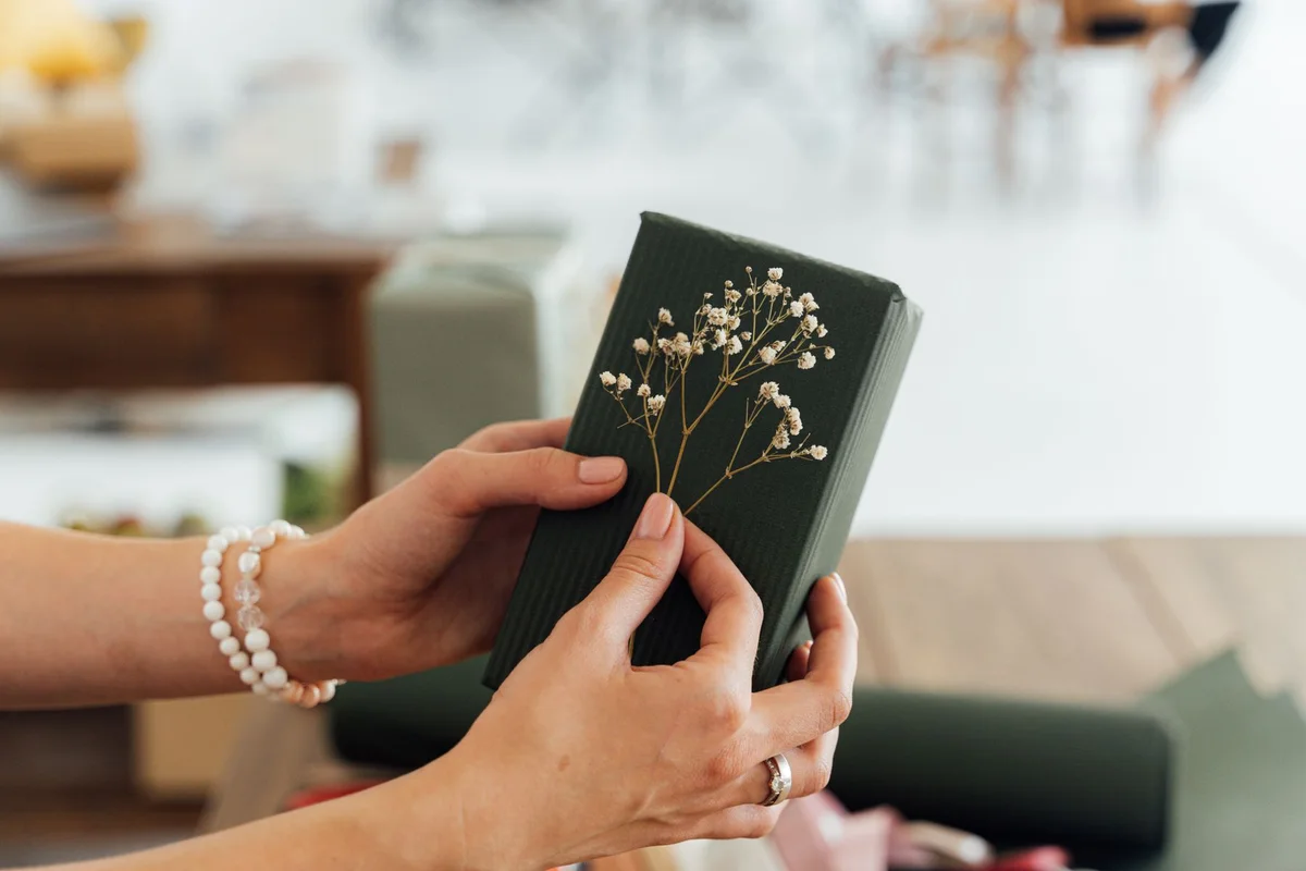 Hands holding a green wrapped gift decorated with small white flowers